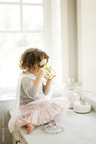 Fotografie Little girl drinking tea in white kitchen
