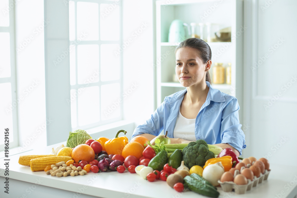 happy young housewife sitting in the kitchen preparing food from a pile of diverse fresh organic fruits and vegetables happy young housewife sitting in the kitchen preparing food from a pile of diverse fresh organic fruits and vegetables