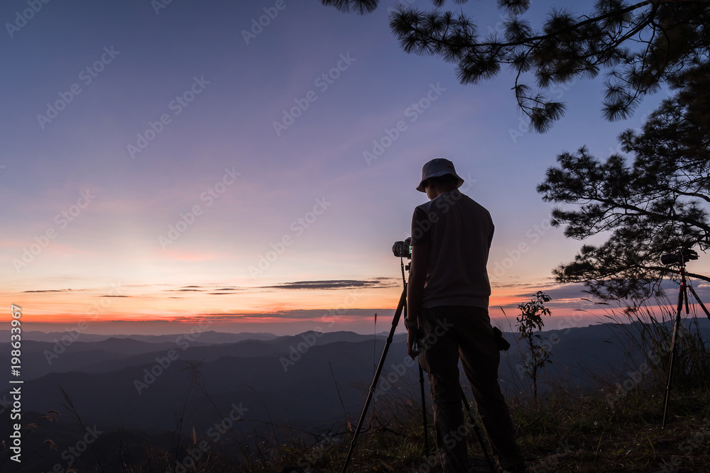 Hiker with camera on tripod takes picture from rocky summit.