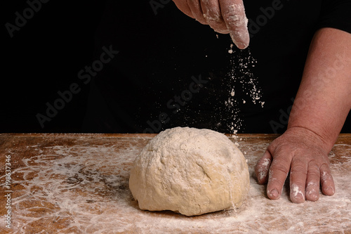 The hands of an old grandmother sprinkle with flour dough