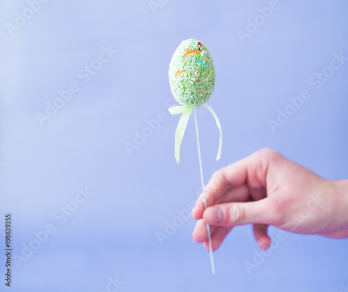 Man holding a green Easter egg on a stick on a blue background photo