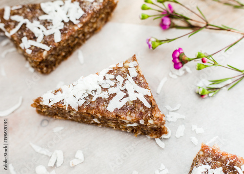 Overhead shot of morning light across raw cacao enery bars on white parchment paper with coconut  on a wooden surface with fresh flowers. photo