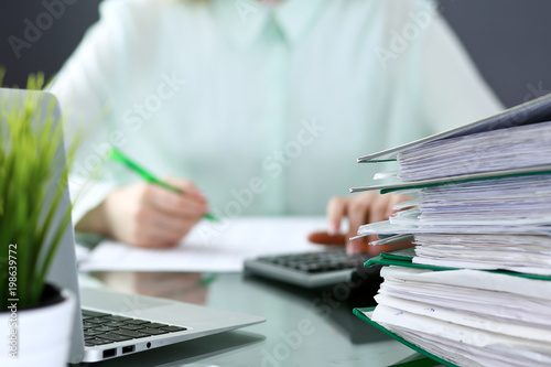 Bookkeeper or financial inspector  making report, calculating or checking balance. Binders with papers closeup. Audit and tax service concept. Green colored image background 