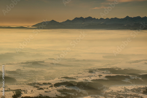 Jagged peaks of mighty High and White Tatra rise above sea of fog in Polish Podhale basin in glowing light at dawn, Tatry Wysokie Zakopane Malopolska Lesser Poland Spis Slovakia Eastern Central Europe