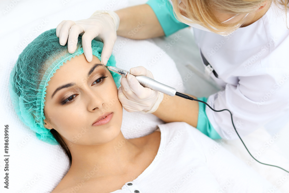 Professional beautician doing eyebrow tattoo at woman face. Permanent brow makeup in beauty salon, closeup.  Cosmetology treatment