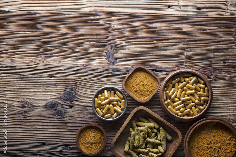 Curcuma capsules, turmeric roots and powder in bowls. Anti cancer medicine. Wooden table. Top view shot.
