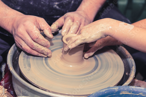 Little child learns how to sculpt a ceramic plate on a potter's wheel. Close-up of a child's hand.