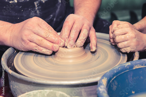 Men's and child's hands. Potter at work. Creating dishes. Potter's wheel. Dirty hands in the clay and the potter's wheel with the product. Creation. Working potter.