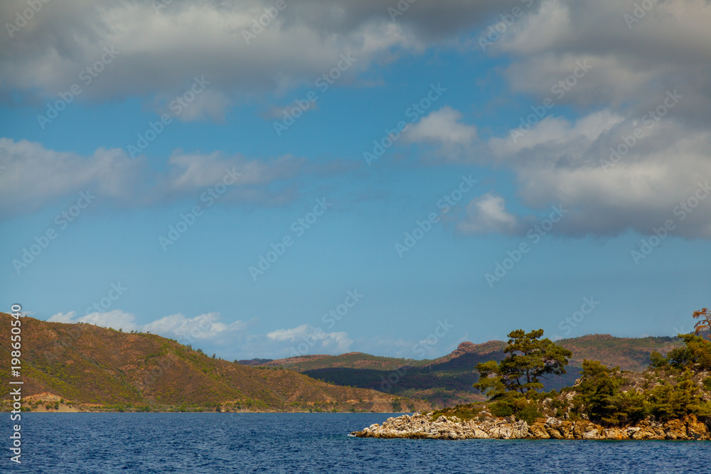 Rocky coast with trees in the Aegean Sea. Big beautiful white clouds