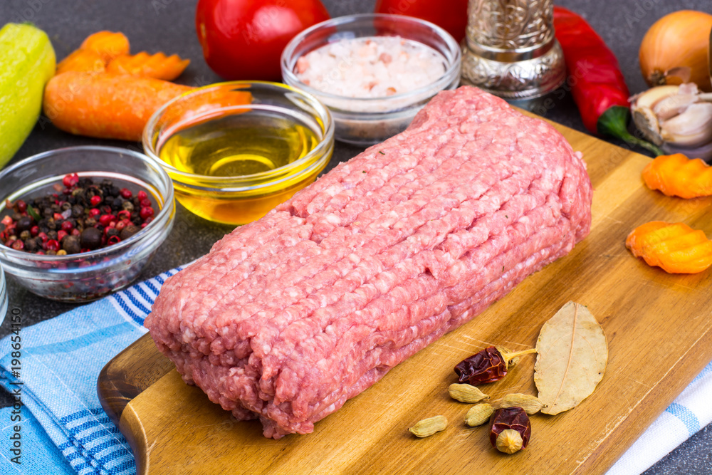 Fresh ground meat on wooden board with spices, vegetables Fresh ground meat on wooden board with spices, vegetables