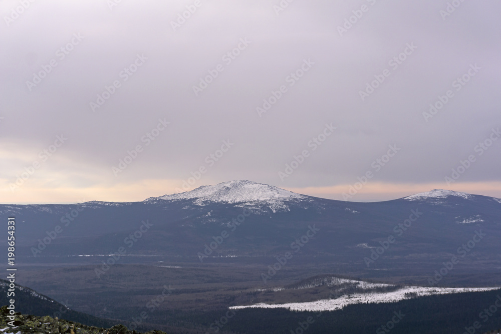 winter wooded mountains with a snow peak or a volcano cone in the distance..