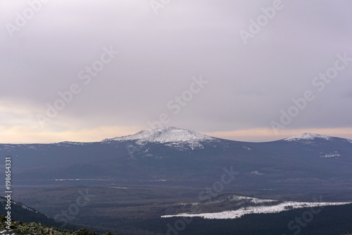 winter wooded mountains with a snow peak or a volcano cone in the distance..