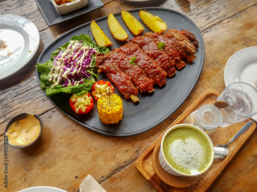 Pork Spare Ribs Barbecue with fried potato and fresh vegetable in black ceramic dish on wooden table