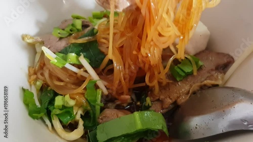 close up chopstick holding traditional ิNoodle Soup Thai Style (Pork or Beef) boat in the bowl.