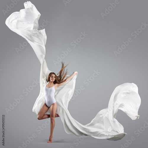 Young attractive girl dancing in the Studio with a white cloth. Fabric flies through the air.