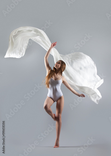 Fototapeta Naklejka Na Ścianę i Meble -  Young attractive girl dancing in the Studio with a white cloth. Fabric flies through the air.