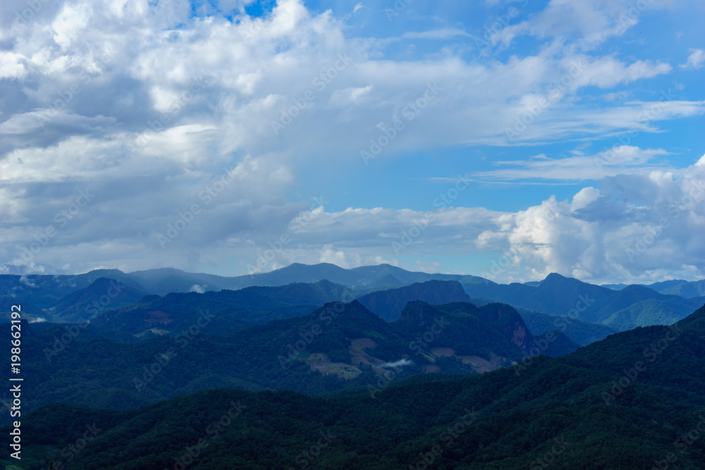 Obraz premium Amazing wild nature view of layer of mountain forest landscape with cloudy sky at winter season. Natural green scenery of cloud and mountain slopes background.