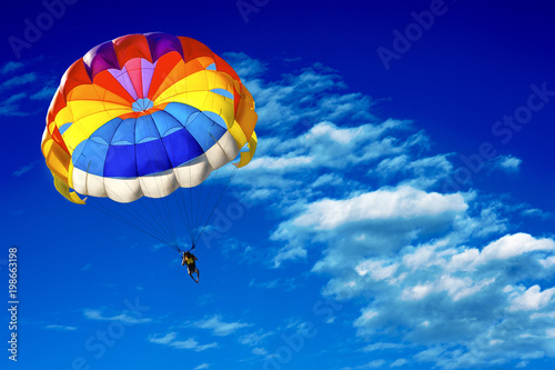 A man is gliding using a parachute on the background of cloudy blue sky. photo