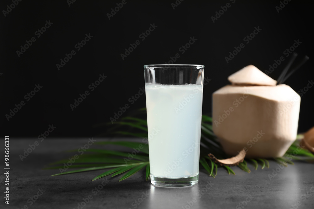 Glass with fresh coconut water on table against black background Glass with fresh coconut water on table against black background