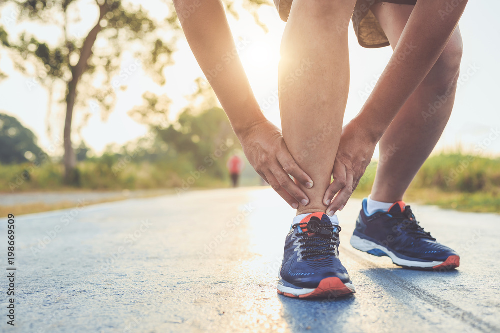 Injury from workout concept : Asian man use hands hold on his ankle while running on road in the park. Focus on ankle.