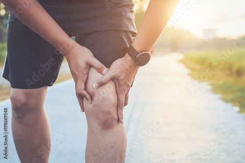 Injury from workout concept : Asian man use hands hold on his knee while running on road in the park. Shot in morning time, sunlight and warm effect with copy space for text or design photo
