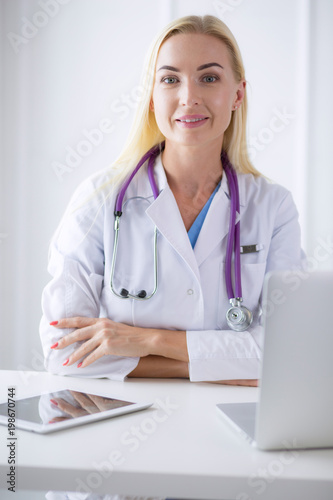 Female doctor sitting on the desk and working a laptop in hospital