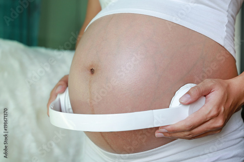 Close-up belly of pregnant woman with headphones.