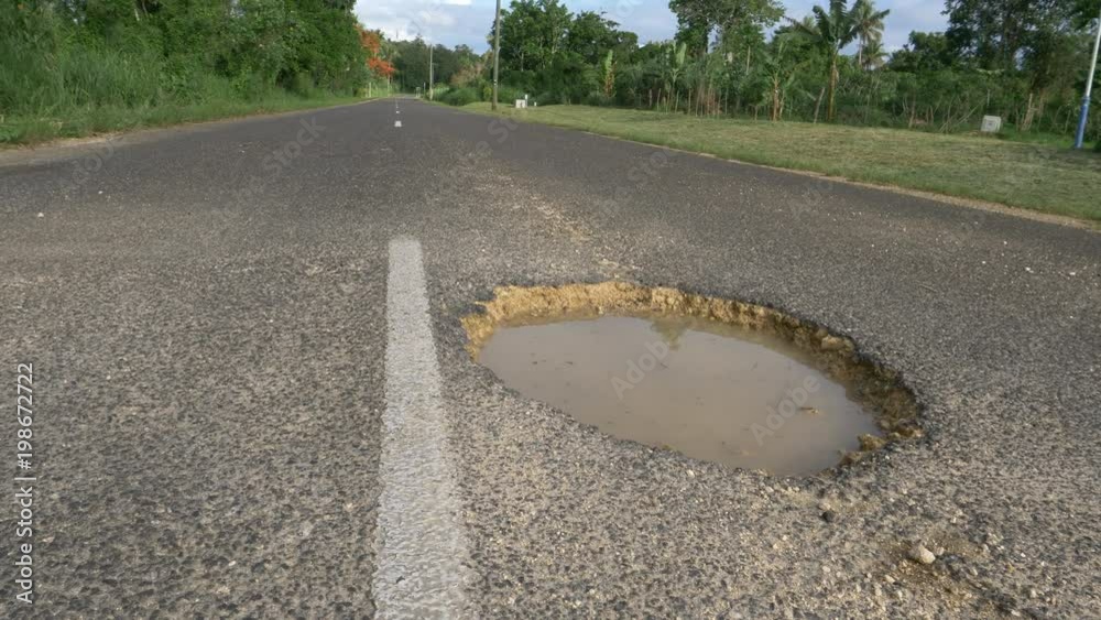 LOW ANGLE, CLOSE UP Large gaping pothole filled with muddy water