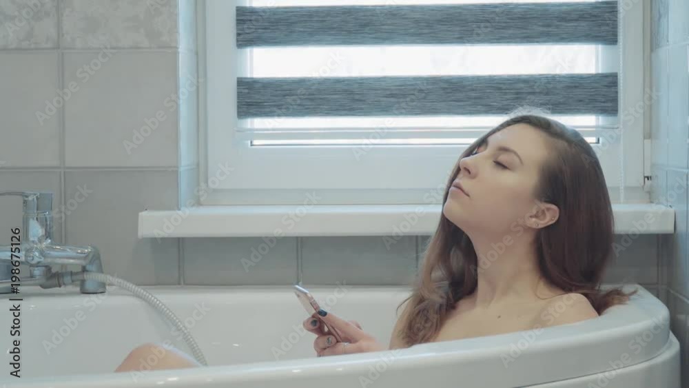 Pretty, young woman wathing in cellphone in bathroom Pretty, young woman wathing in cellphone in bathroom