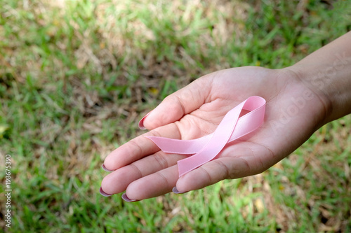 hand of woman holding a pink ribbon Breast Cancer Symptoms Health on the grass and protection concepts © Photo Sesaon