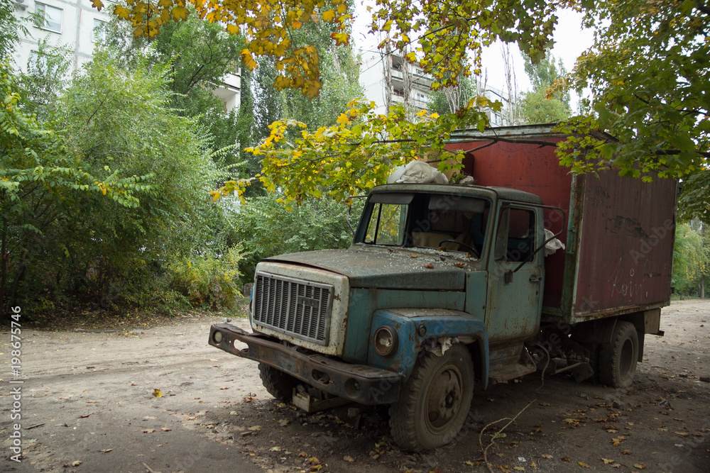Old rusty truck with broken windows at abandoned overgrown part of town