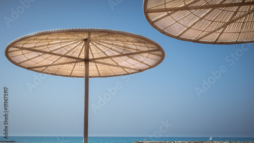 Stylish umbrellas on the city waterfront on background of sea, sky and small sailing boat. Travel summer destination. Tel Aviv city promenade.
