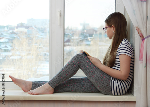 The girl sits on the windowsill and looks out the window.