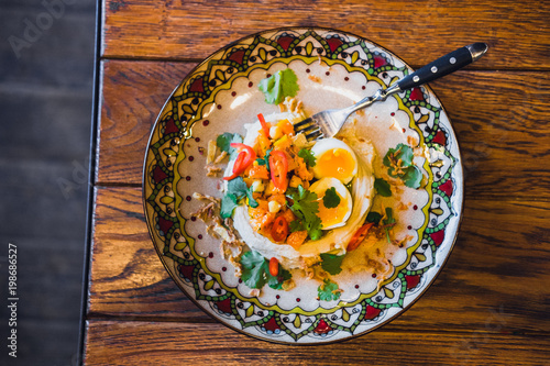 Hummus, baba ghanoush dip with poached eggs, parsley, and chilli. Traditional Middle Eastern appetizer. Colorful ornated plate