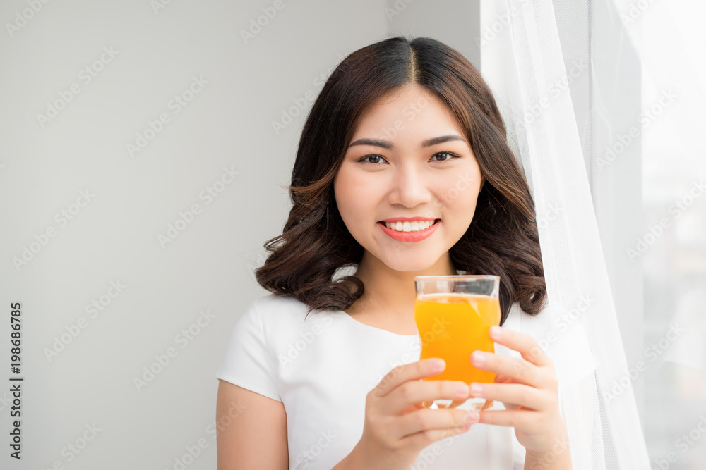 Attractive woman holding a glass of orange juice while standing in the kitchen Attractive woman holding a glass of orange juice while standing in the kitchen