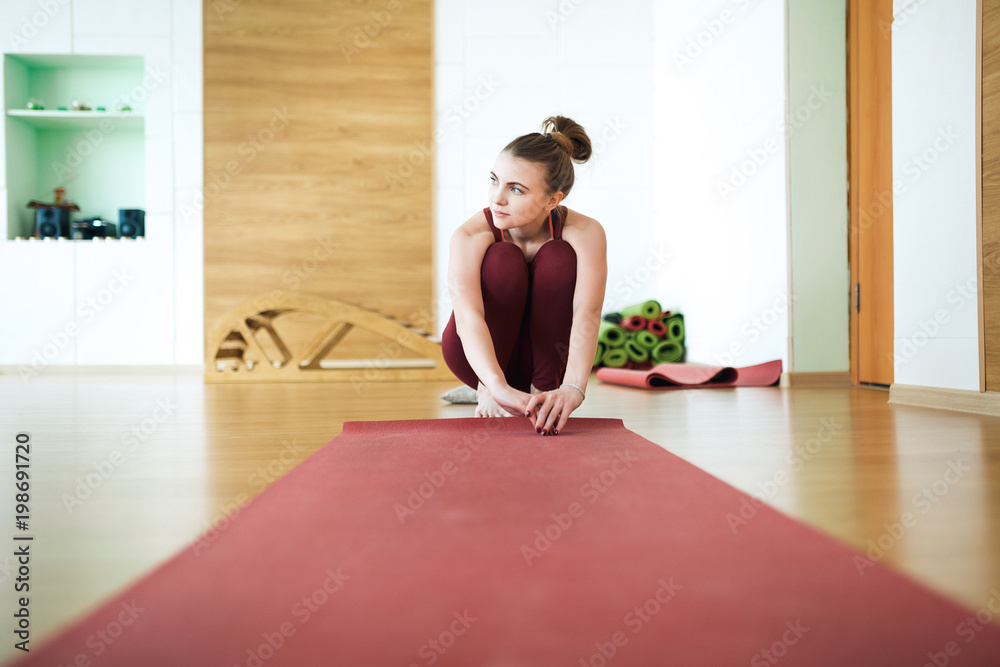 Young attractive woman in a red sportswear in the gym spreads red a yoga Mat. Health concept.The toning. Young attractive woman in a red sportswear in the gym spreads red a yoga Mat. Health concept.The toning.