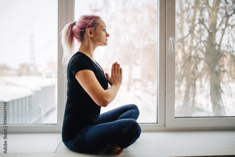 Sensual young girl with pink hair is meditating while sitting in lotus  position near window. Woman holds her hands in Namaste posture, do yoga  lotus position. side view Stock Photo | Adobe