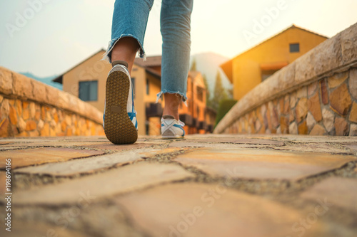 Woman jeans and sneaker shoes walking on the brick bridge to the village with sunlight