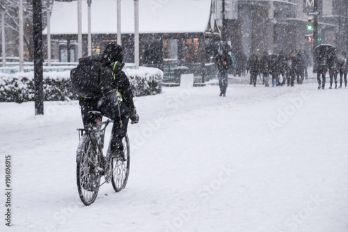 man is riding bicycle in hurry to delivery stuff while it has heavy snow storm on Robson Square, Downtown Vancouver. photo