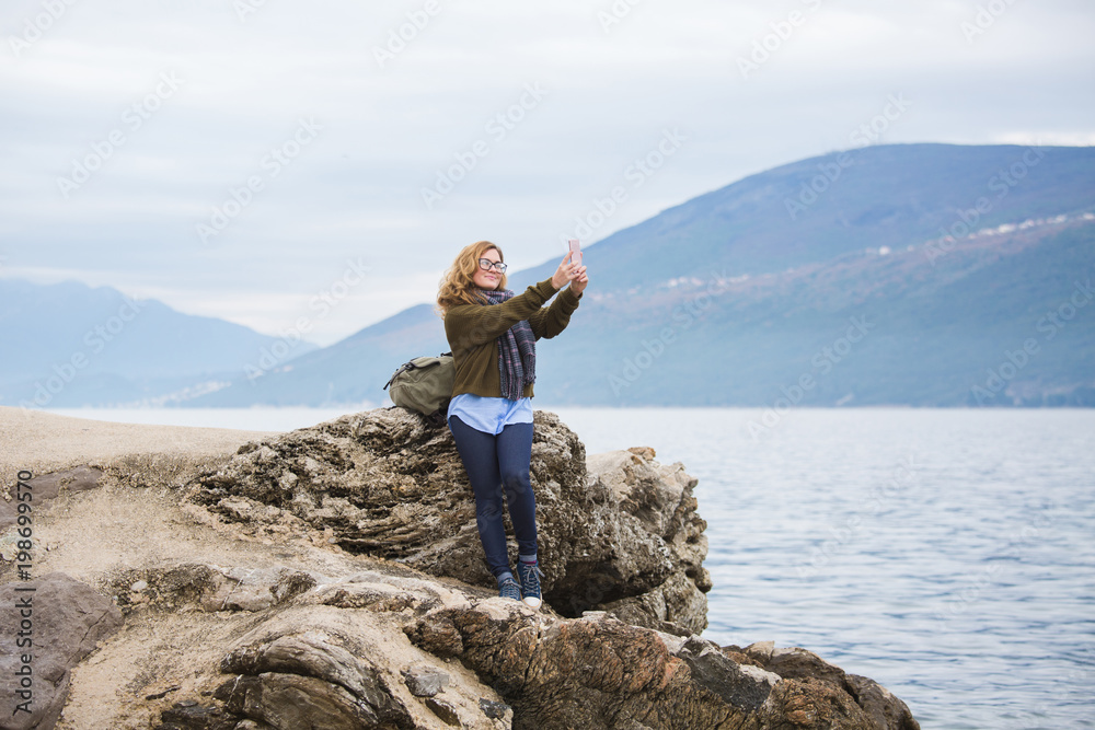 Woman traveler by the sea. On the horizon high mountains. Girl dressed in a sweater and scarf. Woman traveler by the sea. On the horizon high mountains. Girl dressed in a sweater and scarf.