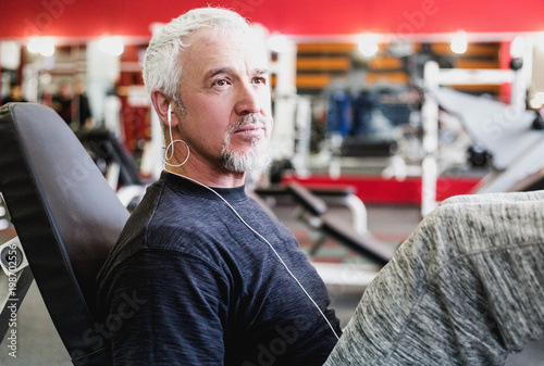 Adult man with gray hair listening to music with headphones in the gym photo