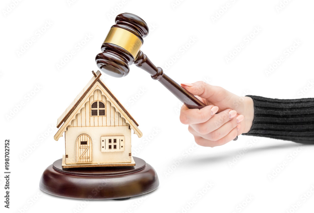 Female's hand holding judge's gavel and model of house on white background. Real estate law concept. House auction.