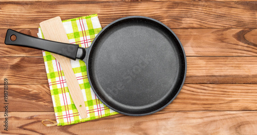 Empty pan with wooden spade and kitchen towel on wooden table. Top view.