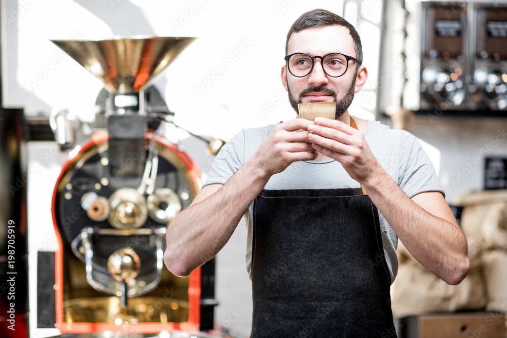 Barista in uniform inhaling the aroma of the coffee standing near the roaster machine in the cafe Barista in uniform inhaling the aroma of the coffee standing near the roaster machine in the cafe