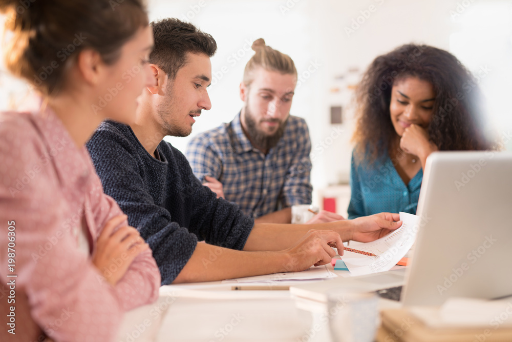At office. Meeting around a table, a young multiethnic team shar At office. Meeting around a table, a young multiethnic team shar
