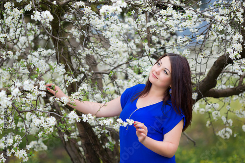 Horizontal portrait of young Caucasian brunette woman near blossoming plum tree  looking up to the sky
