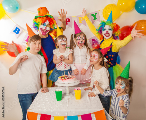 clown girl and clown boy at the children's birthday party. Festive table with a beautiful cake. Blow out candles and make a wish