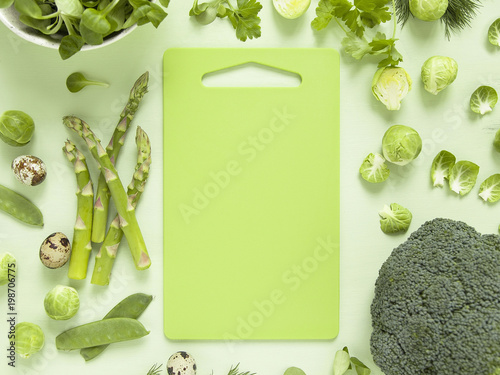 Fresh green vegetables, herbs, lettuce and quail eggs with bright  cutting board in the middle. Spring food concept. 