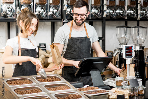 Two sellers in uniform filling bags with coffee beans while working in the coffee store photo