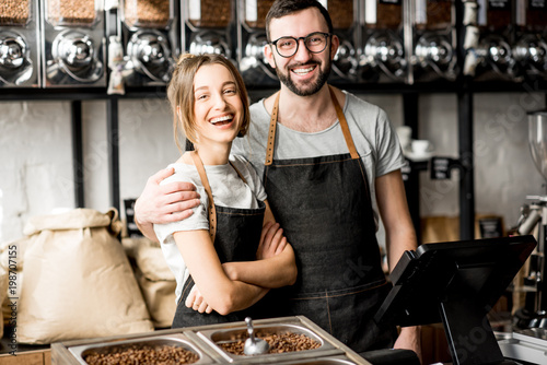 Portrait of a young couple of baristas standing together at the counter of the coffee store photo